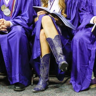 A TCU graduate wears purple cowboy boots with her commencement gown
