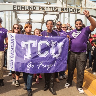  A group TCU students walks across the Edmund Pettus Bridge in Selma, Alabama. They hold a TCU flag and several students make the wo-fingered Go Frogs hand gesture.