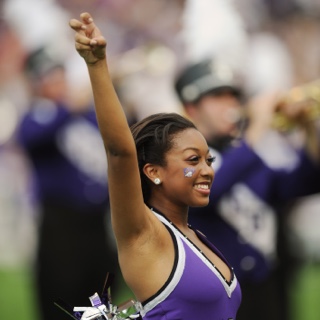 A smiling TCU Showgirl makes the two-fingered "Go Frogs" hand sign at a crowded football game.