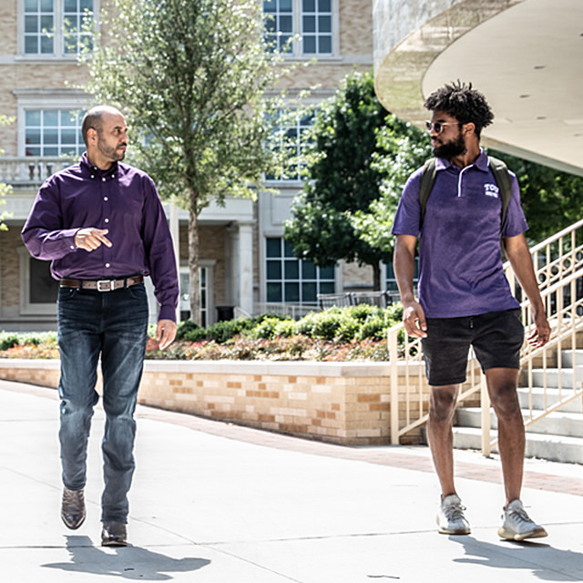 TCU professors chatting with a student as they walk across campus