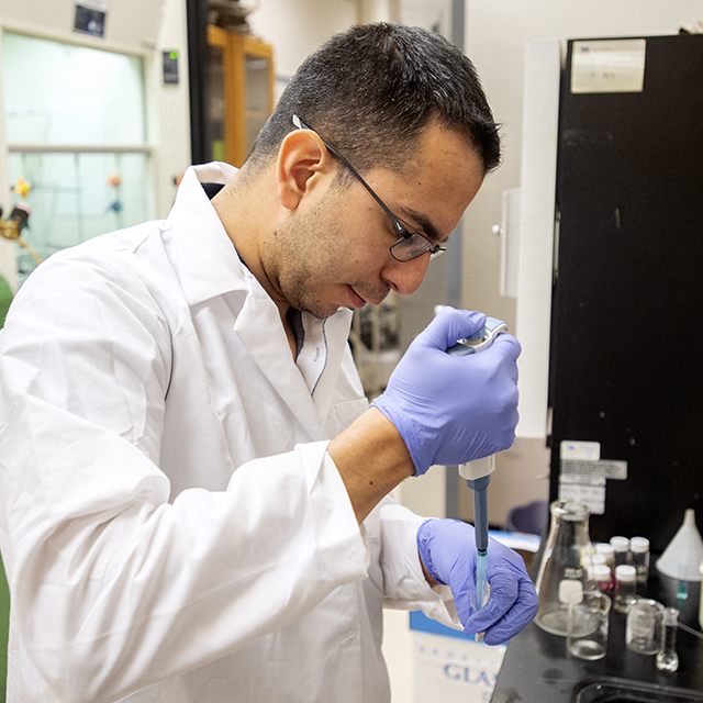 A graduate student carefully meters material into a test tube