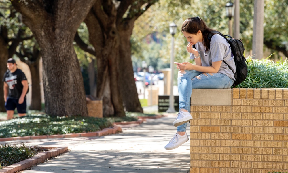 female student on campus sitting on a wall