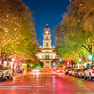 A northerly view at night looking up a downtown street lined with trees adorned with sparkling white lights to the county courthouse