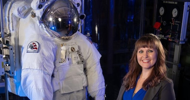 A person poses next to an astronaut suit.