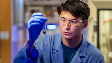 Chemistry student in lab coat and safety goggles examines content of a test tube