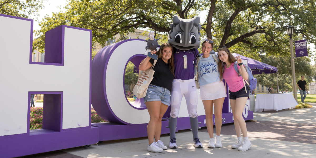 students with SuperFrog in front of Home sign